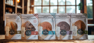 Five packages of different types of bread on a wooden surface with a blurred indoor background.