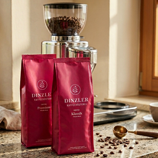 Two red Dinzler coffee bags on a kitchen counter with a coffee grinder and beans.