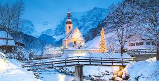 Snowy village scene with a church and Christmas lights in the mountains